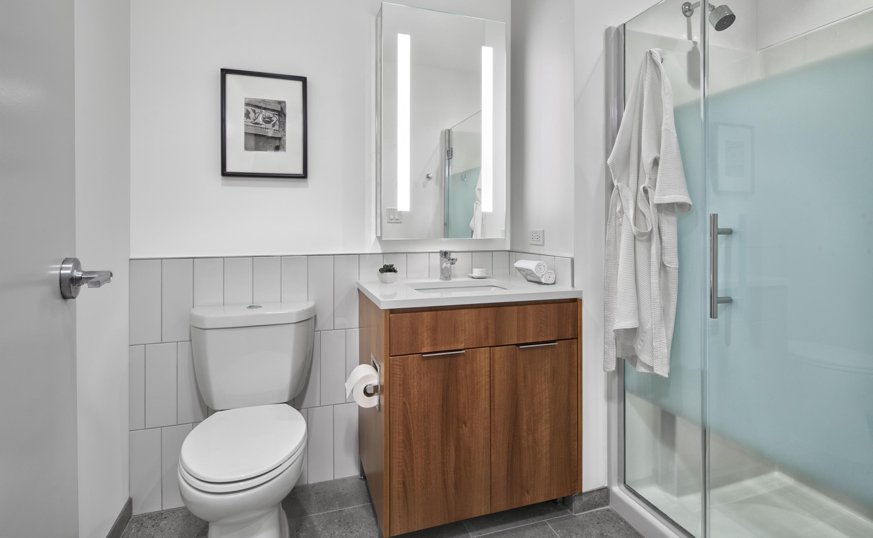 Sample bathroom with tiled flooring, toilet, vanity with under-sink cabinetry, and a walk in shower with glass door