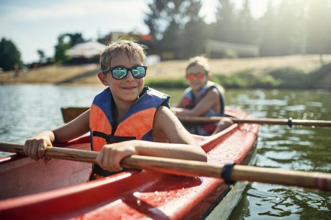 Two young boys wearing sunglasses and life jackets as they enjoy kayaking on lake on a sunny summer day.