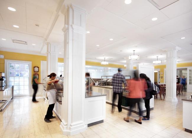 People wandering about a buffet-style dining hall serving themselves food.