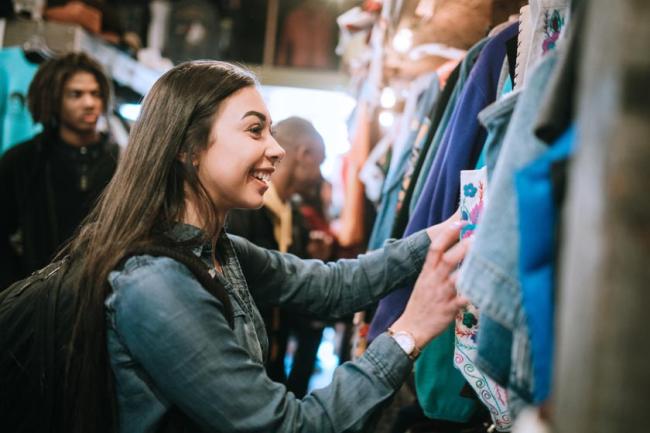 A smiling group of young adults shopping for retro and vintage clothing styles at a second hand thrift store.