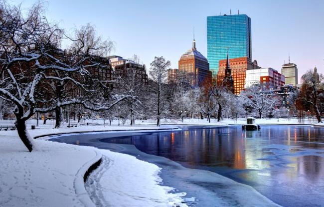 The Boston Public Garden in Massachusetts covered in snow, with a frozen pond that is icy blue.