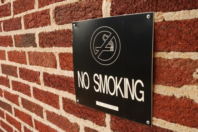 A black No smoking sign attached to a brick wall.