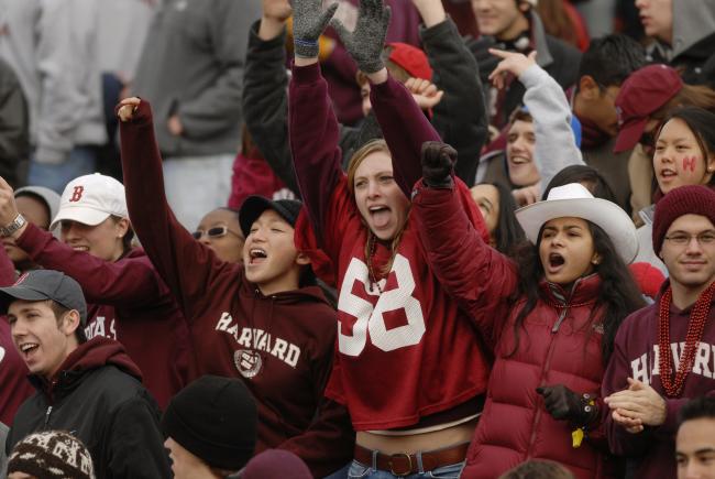 A group of Harvard students in the stands, cheering during an athletics game.