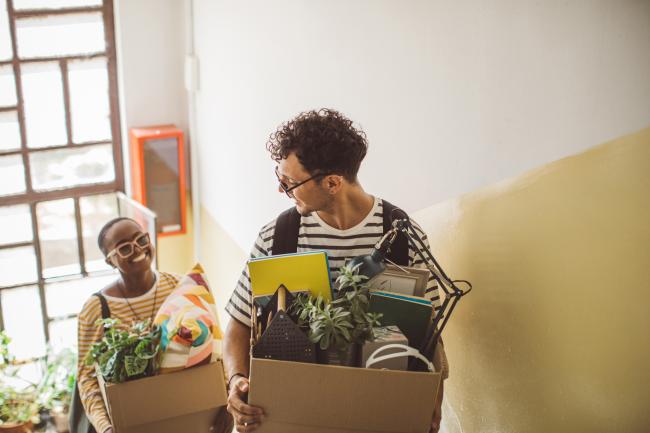 two people moving boxes of belongings up the stairs, smiling at eachother