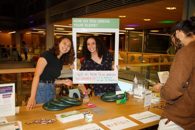 Two people at a sustainability event smiling for the camera and posing in a frame