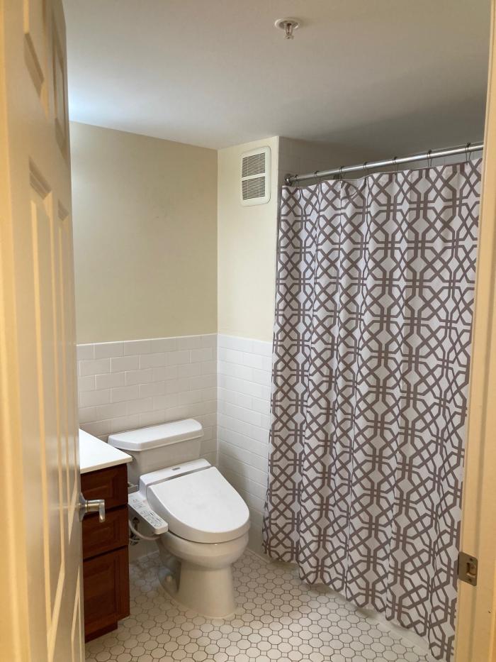 Bathroom with white toilet and tub/shower, white tile, and a white sink counter. Sink has brown cabinetry.
