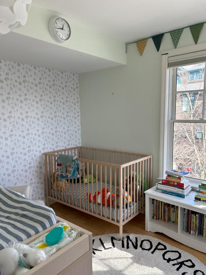 a nursery bedroom with off white walls and one patterned wall. Hardwood floors.