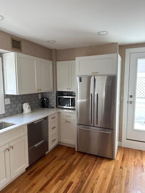 Stainless steel kitchen fridge with white cabinets, grey backsplash, and white countertops