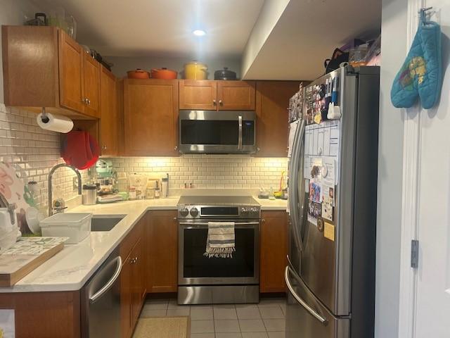 kitchen with stainless steel appliances, white countertops, wooden cabinetry, and tiled flooring.