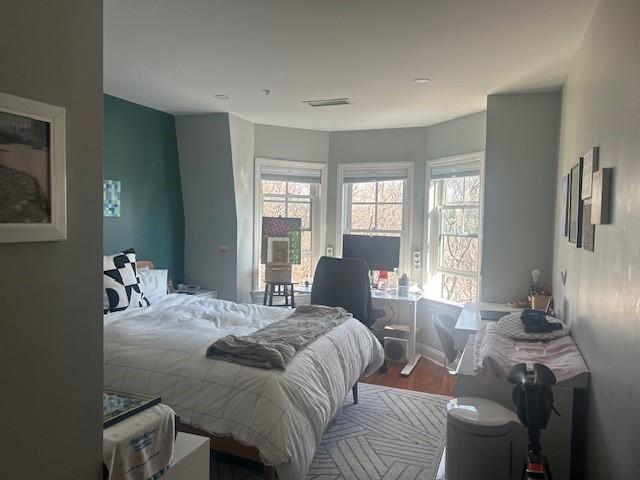 Primary bedroom with bay windows, hard flooring, and pale blue grey walls.