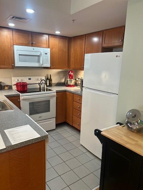 kitchen with white appliances, tile flooring, grey countertops, and wooden cabinetry