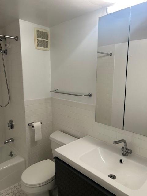 Primary bathroom with tile flooring, white toilet, shower/tub, sink and vanity