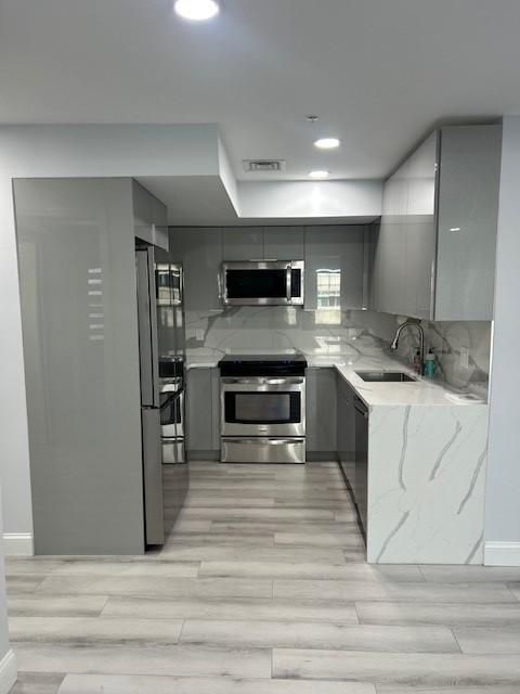 Kitchen with stainless steel appliances, grey cabinetry, light wood plank floors and white countertops