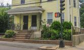 A yellow multifamily building located by a crosswalk. There is a small porch and landscaping surrounding the property.