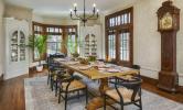 A large dining room with a long dining table and chairs, with large windows and a grandfather clock.